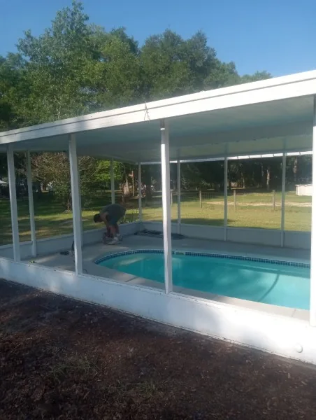 White-framed pool screen enclosure with a person working beside the pool