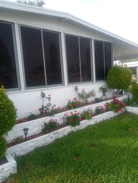 White-framed screened room exterior with a landscaped garden