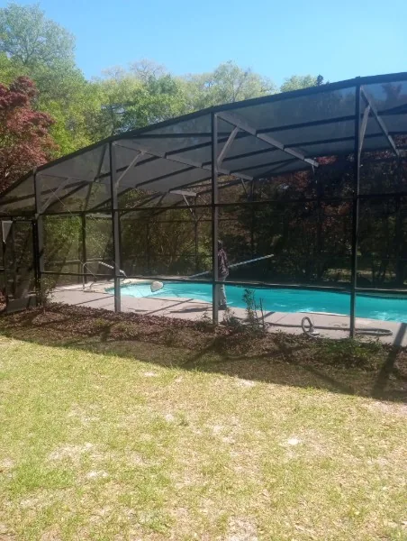 Dark-framed screened swimming pool enclosure beside a lawn